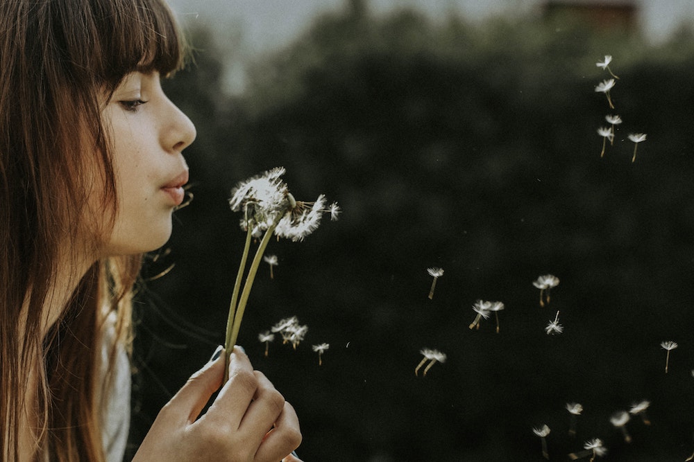 Young woman blowing dandelion seeds into the air